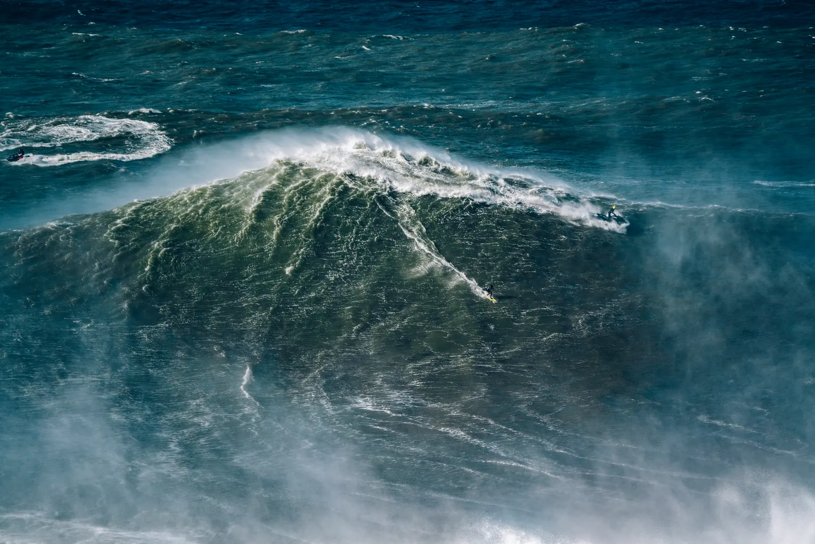 A surfer and safety team on a giant Nazaré wave.